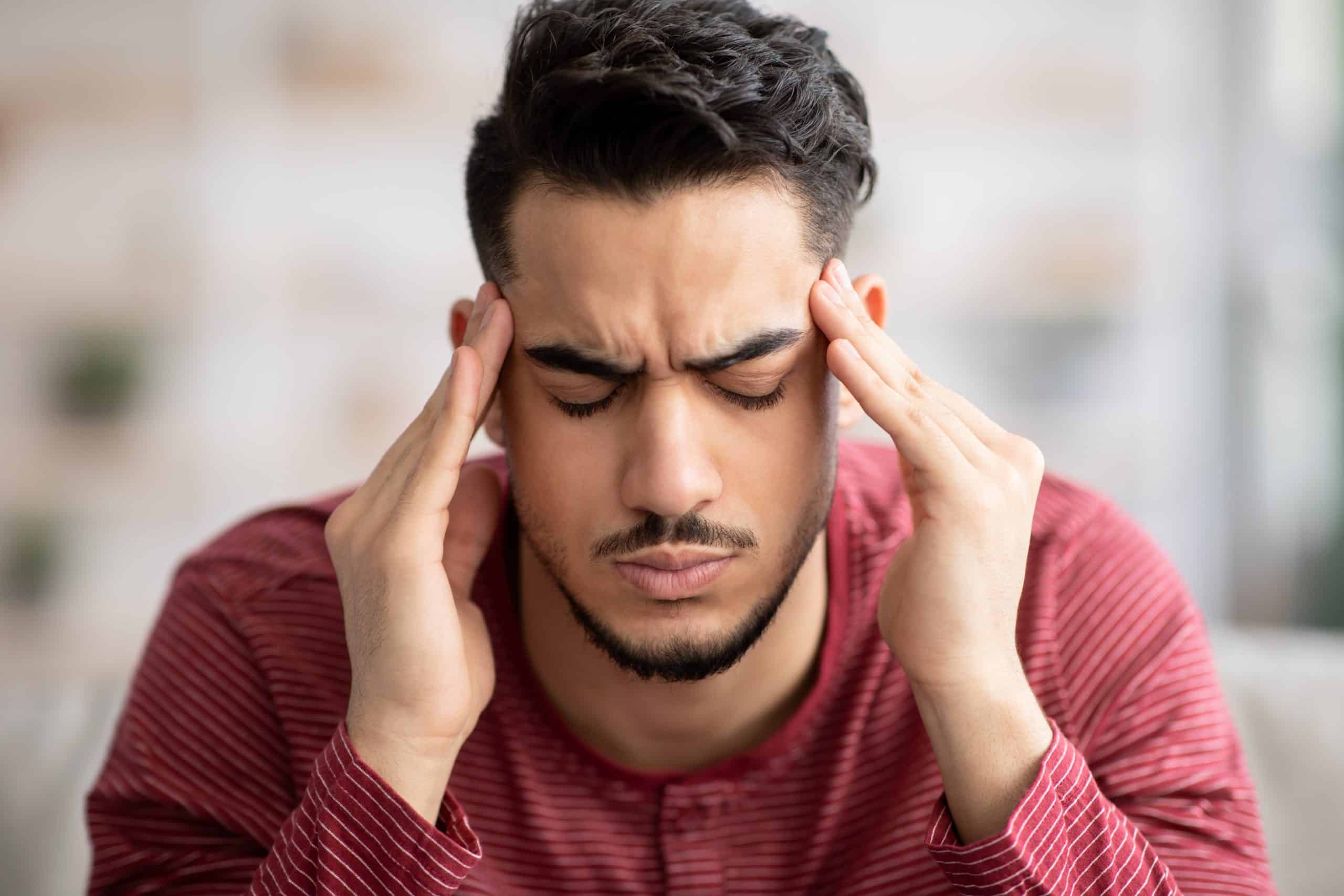Closeup of bearded arab guy suffering from migraine at home, touching his temples with closed eyes, copy space. Migraine, headache, stress, tension problem, hangover concept