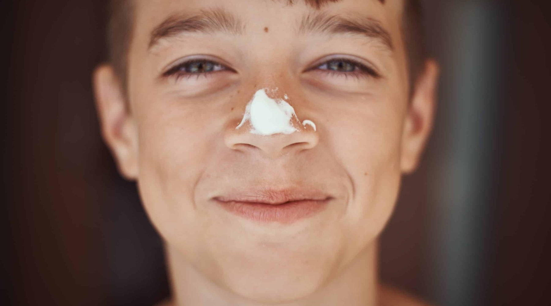 Happy smile boy with sunscreen cream on nose, close up portrait. Summer holidays and vacation concept