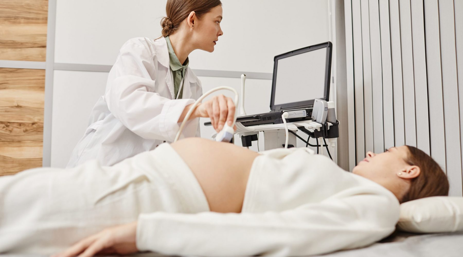 Portrait of female doctor performing ultrasound exam on pregnant young woman in modern medical clinic