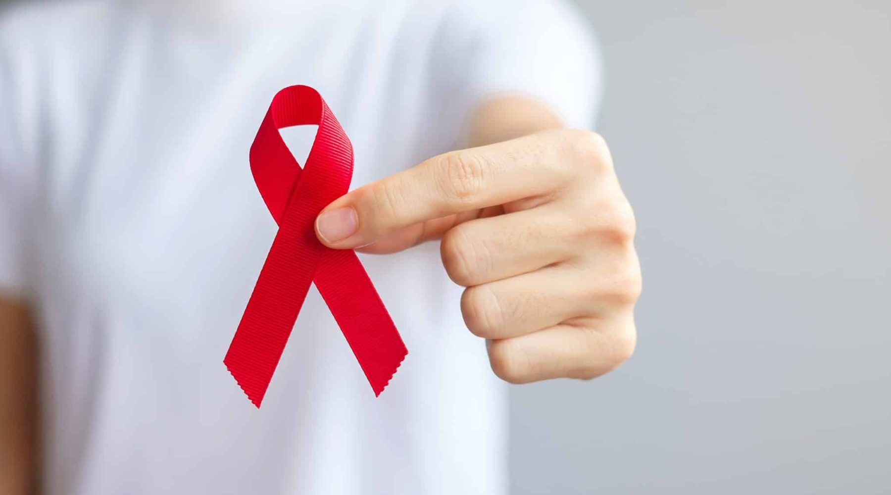 Hand holding Red Ribbon for December World Aids Day (acquired immune deficiency syndrome), multiple myeloma Cancer Awareness month and National Red ribbon week. Healthcare and world cancer day concept